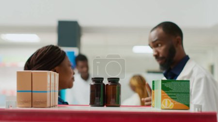 Téléchargez les photos : Consultant afro-américain donnant boîte de pilules à la femme, recommandant de bons médicaments pour guérir la maladie. Jeune client demandant conseil à un pharmacien, pharmacie. Trépied. - en image libre de droit