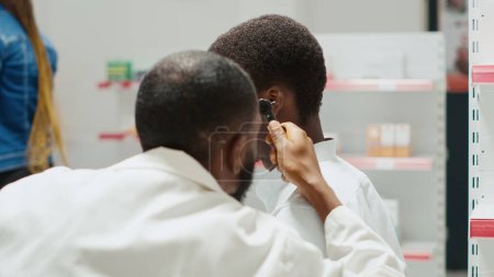 Photo for Pharmacy worker consulting man with otoscope tool, otologist doing consultation and ear examination in drugstore center. Young doctor doing otology checkup with male client. Handheld shot. - Royalty Free Image