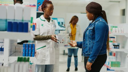 Photo for Woman pharmacist helping customer with medication in pharmaceutical shop. Young adult talking to pharmacy assistant about prescription treatment and vitamis, boxes of drugs. Handheld shot. - Royalty Free Image