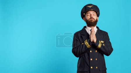 Téléchargez les photos : Spiritual aircrew captain praying to god in studio, being religious and worshiping christ. Male airline pilot showing prayer hands gesture on camera, asking for forgiveness and having faith. - en image libre de droit
