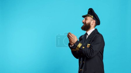 Photo for Male aviator applauding and cheering on camera, saying congratulations and clapping hands in studio. Airline pilot in flying uniform with cheerful emotions doing standing ovation sign. - Royalty Free Image