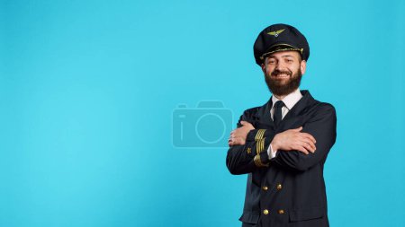 Téléchargez les photos : Portrait d'un commandant de bord souriant posant à la caméra, agissant positivement et confiant avec l'uniforme d'aviation. Pilote ayant une occupation professionnelle pour le transport aérien, avion volant. - en image libre de droit