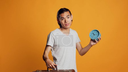 Photo for Male person carrying suitcase and checking time on clock, preparing to leave with briefcase and running late. Stressed young man being in a hurry and looking at watch, holding bag. - Royalty Free Image