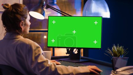Photo for Business woman analyzing green screen display on pc, looking at computer with chroma key isolated template. Female employee working overtime with blank mockup screen, copyspace. - Royalty Free Image