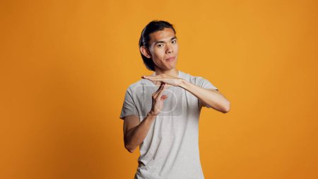 Photo for Young adult doing t shape symbol on camera, showing break or pause sign for denial and refusal. Asian casual guy expressing rejection and asking for half time, body language concept. - Royalty Free Image