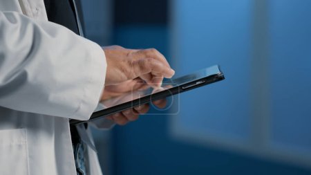 Photo for Close up of general practitioner holding tablet computer searching for patient disease report before start planning medication treatment in hospital office. Medical team working night shift - Royalty Free Image