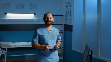 Photo for Caucasian man assistant holding tablet computer typing medical expertise checking patient disease report. Nurse in blue uniform working after hours in hospital office. Health care service and concept - Royalty Free Image