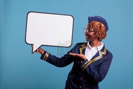 Photo for African american female flight attendant holding speech balloon. Smiling air hostess studio portrait with banner next her. Uniformed stewardess holding dialogue window. - Royalty Free Image