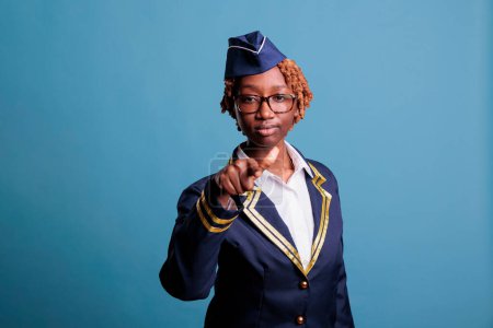 Photo for Serious african american, curly hair air hostess, studio portrait, pointing straight at camera. Female flight crew member hiring, employing, looking for new personnel. - Royalty Free Image
