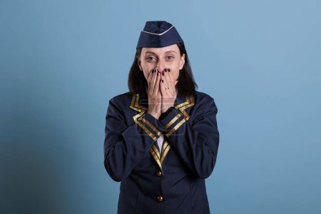 Foto de Flight attendant covering mouth with hands, showing speak no evil gesture, looking at camera. Airplane stewardess with covered lips front view, censorship, keeping silence concept - Imagen libre de derechos