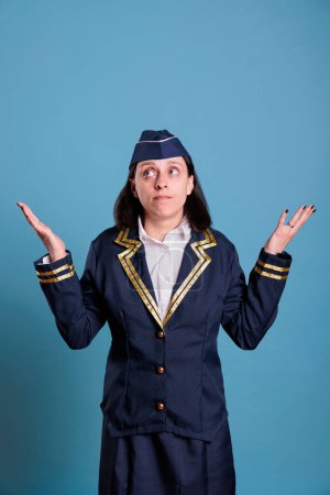 Photo for Young confused stewardess shrugging shoulders, showing unsure gesture, looking upwards. Flight attendant with doubtful facial expression, puzzled air hostess, uncertain sign - Royalty Free Image