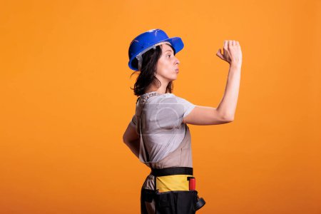 Photo for Female builder supervising renovation project, wearing overalls and protective helmet. Construction worker expert looking at building site and checking refurbishment work in studio. - Royalty Free Image
