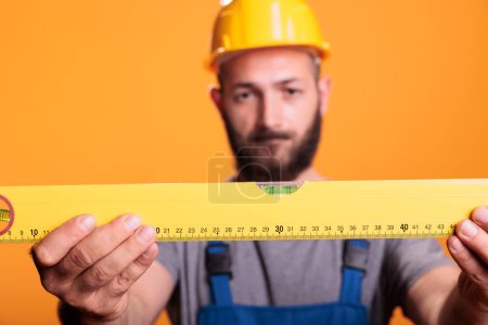 Photo for Focused foreman expert looking at construction leveler before working on refurbishment project, studio shot. Handyman builder carrying water level tool or ruler to work on renovation. - Royalty Free Image