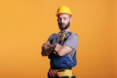 Photo for Craftsman engineer using hammer on renovation project, standing over yellow background. Professional male renovator doing reconstruction work with sledgehammer and tools, studio shot. - Royalty Free Image