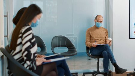 Photo for Female employee taking african american man to attend meeting with HR department. Multiethnic group of candidates waiting to join job interview during coronavirus pandemic in office. - Royalty Free Image