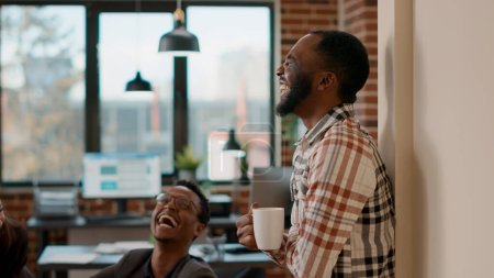 Téléchargez les photos : Homme afro-américain riant et parlant à des collègues de travail, discutant de leadership et de gestion de projet. Heureux gens d'affaires se réunissent pour faire du travail de collaboration. Coup de main. - en image libre de droit