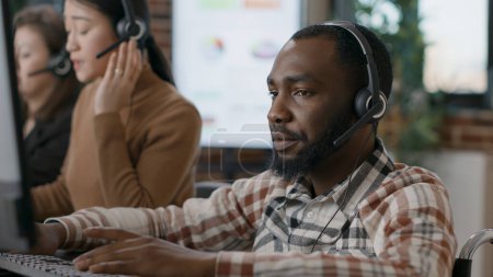Young man answering telework call at customer service job, talking to clients on phone helpline. Male worker using audio headset to given assistance and support to people. Close up.