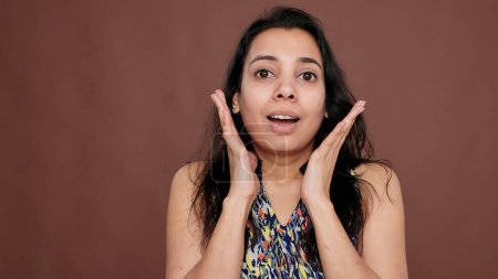 Photo for Surprised woman raising hands and being shocked on camera, showing excitement and astonishment. Pretty joyful person expressing positive emotions and feeling amazed by news in studio. - Royalty Free Image