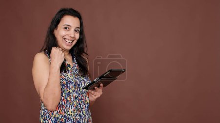 Photo for Indian person using digital tablet to achieve success, feeling proud while she browses through internet website app. Portable device with touchscreen to scroll on social media network. - Royalty Free Image
