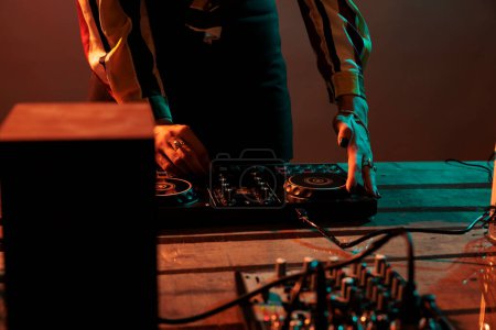 Téléchargez les photos : Musical artist mixing techno music on turntables, playing record mix sounds on audio dj instrument and stereo equipment. Enjoying nightclub party with stage production on studio background. - en image libre de droit