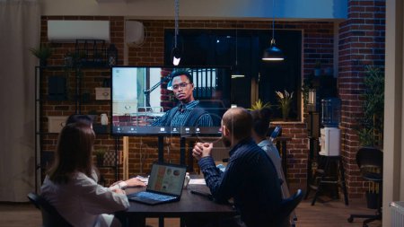 Photo for Employees talking with team leader in remote business meeting videocall zoom in, diverse people talking in videoconference at night time. Office workers chatting in teleconference - Royalty Free Image
