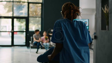 Photo for Assistant helping adult in wheelchair to meet with family in hospital lobby, old patient dealing with physical impairment at facility. Mother and child visiting senior person in waiting room. - Royalty Free Image