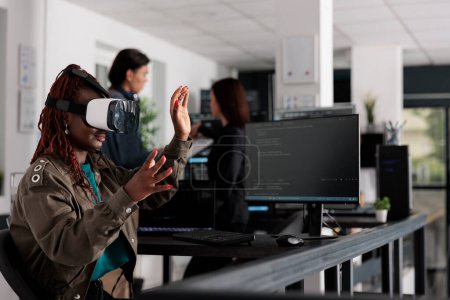 Téléchargez les photos : African american system engineer wearing virtual reality goggles working to develop security program in it big data office, software developer with vr headset coding html script with database. - en image libre de droit