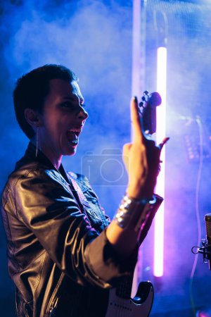 Téléchargez les photos : Woman superstar with short hair holding electric guitar playing rock music preparing heavy song to perform at grunge concert. Rockstar in leather jacket adjusting electricinstrument working at - en image libre de droit