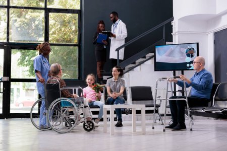 Photo for Medical assistant discussing disease expertise with family explaining health care treatment during checkup visit in hospital reception. Elderly woman in wheelchair finising consultation - Royalty Free Image