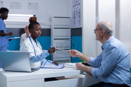 Photo for Healthcare medical expert handing discharge documents to healthy retired patient while talking about treatment side effects. General practitioner specialist discussing with senior about medical - Royalty Free Image