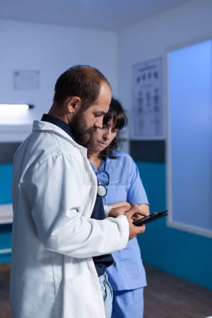 Photo for Medic and assistant working with digital tablet for healthcare at night shift. Medical nurse and doctor using gadget with touch screen, working late in office. People looking at screen - Royalty Free Image
