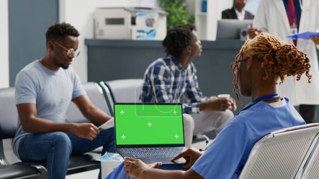 Téléchargez les photos : Infirmière afro-américaine regardant un ordinateur portable avec écran vert, analysant l'affichage chromatique clé dans la salle d'attente. Spécialiste travaillant avec un modèle de maquette vierge et un espace de copie isolé, les soins de santé. - en image libre de droit