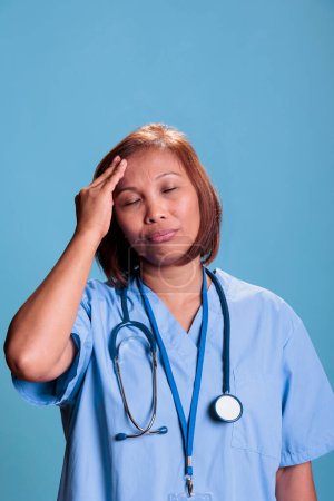 Photo for Tired nurse having migraine while working at medical expertise during checkup visit appointment, portrait. Depressed sick assistant suffering from headache. Health care service and concept - Royalty Free Image