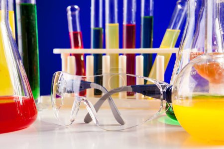 Téléchargez les photos : Laboratoire de chimie avec des produits chimiques colorés sur une table sur fond bleu. Verrerie et matériel de biologie - en image libre de droit