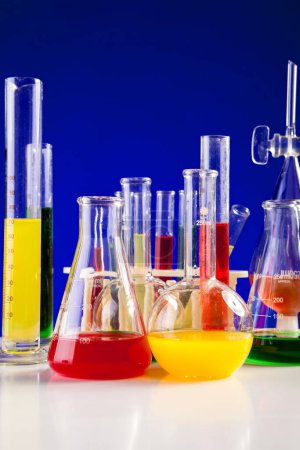 Téléchargez les photos : Laboratoire de chimie avec des produits chimiques colorés sur une table sur fond bleu. Verrerie et matériel de biologie - en image libre de droit