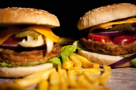 Foto de Classic cheeseburgers on wooden plate next to fries. Fast food. Unhealthy snack - Imagen libre de derechos