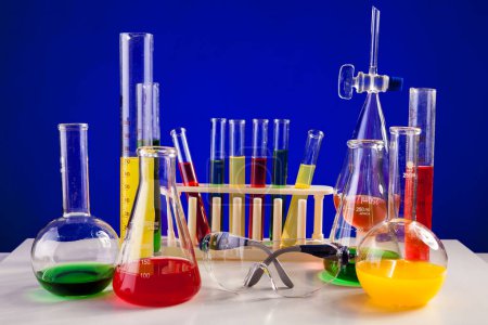 Téléchargez les photos : Chemistry lab set with colored chemicals in it on a table over blue background. Glassware and biology equipment - en image libre de droit