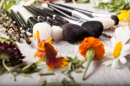 Téléchargez les photos : Cosmétique Brosses de maquillage à côté de fleurs sauvages sur fond en bois - en image libre de droit