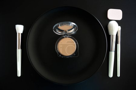 Foto de Imagen conceptual de los pinceles de maquillaje junto al plato de la cena sobre fondo negro - Imagen libre de derechos