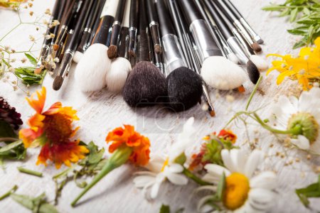 Photo for Cosmetic Make up brushes next to wild flowers on wooden background - Royalty Free Image