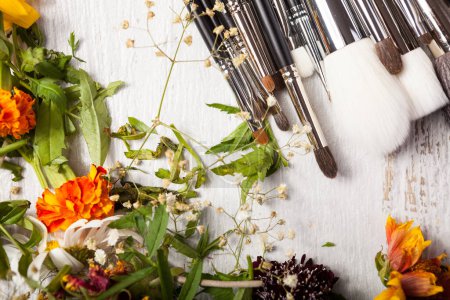 Téléchargez les photos : Cosmetic Make up brushes next to wild flowers on wooden background - en image libre de droit