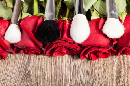 Photo for Conceptual image of make-up brushes next to roses on wooden background - Royalty Free Image