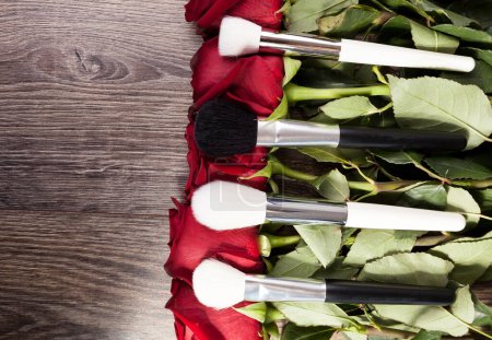Téléchargez les photos : Conceptual image of make-up brushes next to roses on wooden background - en image libre de droit