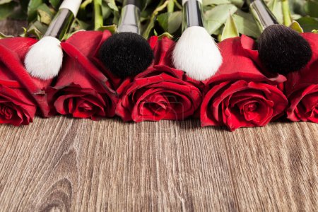 Téléchargez les photos : Image conceptuelle des pinceaux de maquillage à côté des roses sur fond en bois - en image libre de droit