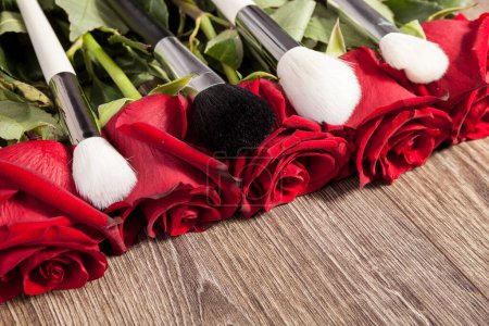Photo for Conceptual image of make-up brushes next to roses on wooden background - Royalty Free Image