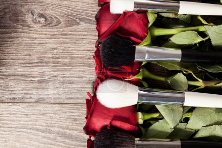 Téléchargez les photos : Conceptual image of make-up brushes next to roses on wooden background - en image libre de droit