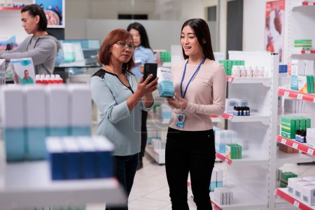 Foto de Pharmacist working in medical shop with elderly customer, helping woman to find prescription drugs box on pharmacy shelves. Client asking specialist about pills in pharmaceutical drugstore. - Imagen libre de derechos