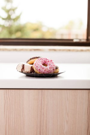 Photo for Plate with donuts next to window sill. Delicious junck food - Royalty Free Image