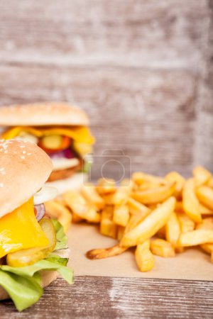 Foto de Sabrosas hamburguesas caseras en plato de madera al lado de papas fritas. Comida rápida. Snack malsano - Imagen libre de derechos