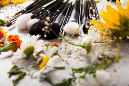 Téléchargez les photos : Make up brushes on a table next to wild flowers on wooden background - en image libre de droit